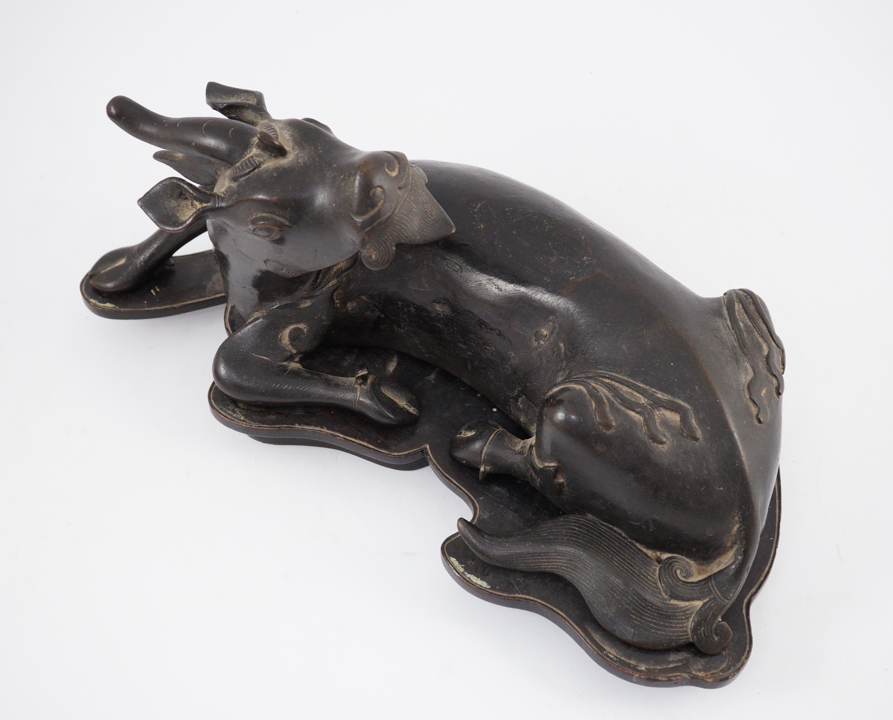 A Chinese bronze figure of a recumbent qilin, late Ming dynasty, 36cm long, old repairs and later base panel, wood stand